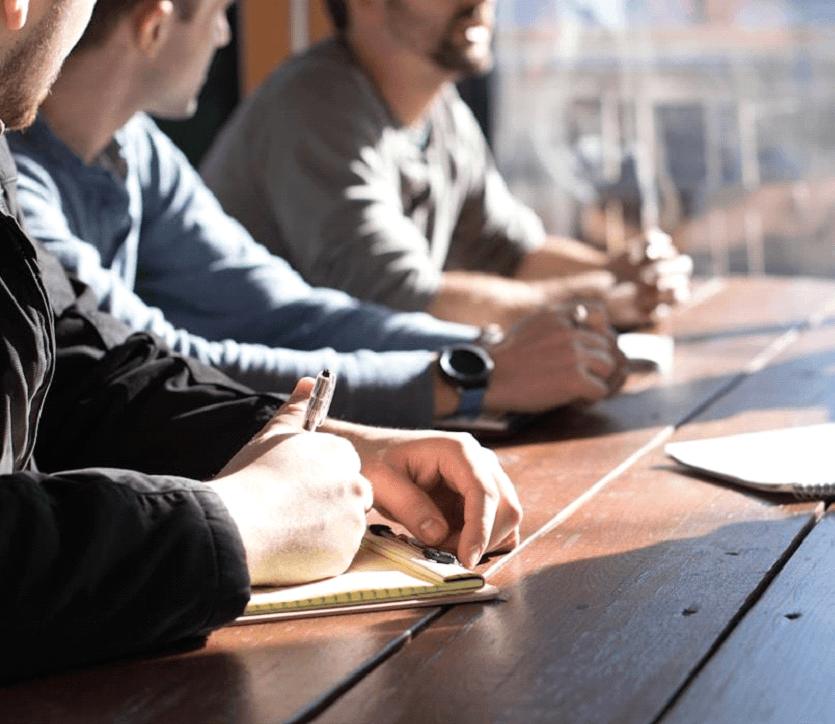 Team members working together at a computer, writing about the benefits of using opportunity management software for sales teams
